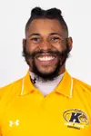 Headshot of Pat Walker smiling broadly, wearing a gold Kent State Football Under Armour polo shirt with the Golden Flashes logo and white collar trim, with a full beard and hair pulled up.