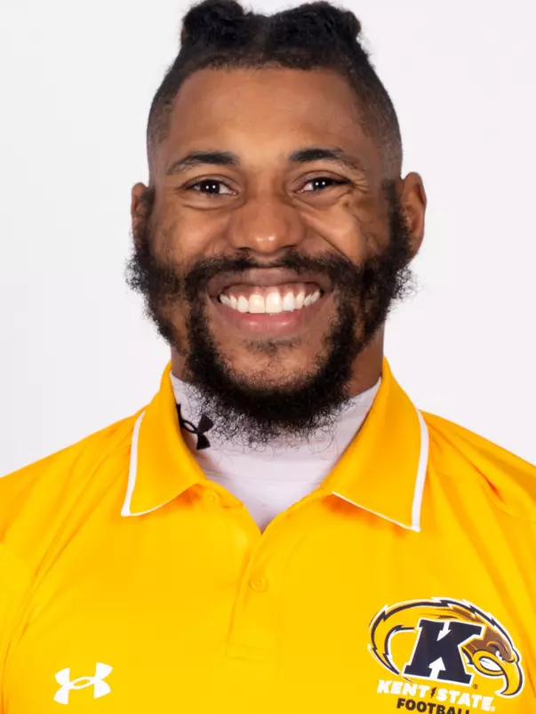 Headshot of Pat Walker smiling broadly, wearing a gold Kent State Football Under Armour polo shirt with the Golden Flashes logo and white collar trim, with a full beard and hair pulled up.