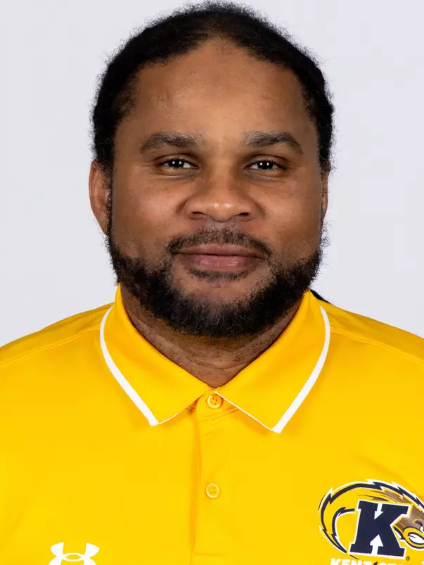 Headshot of Josh Cribbs smiling, wearing a gold Kent State Football Under Armour polo shirt with the Golden Flashes logo and white collar trim, with short dark hair and light stubble.