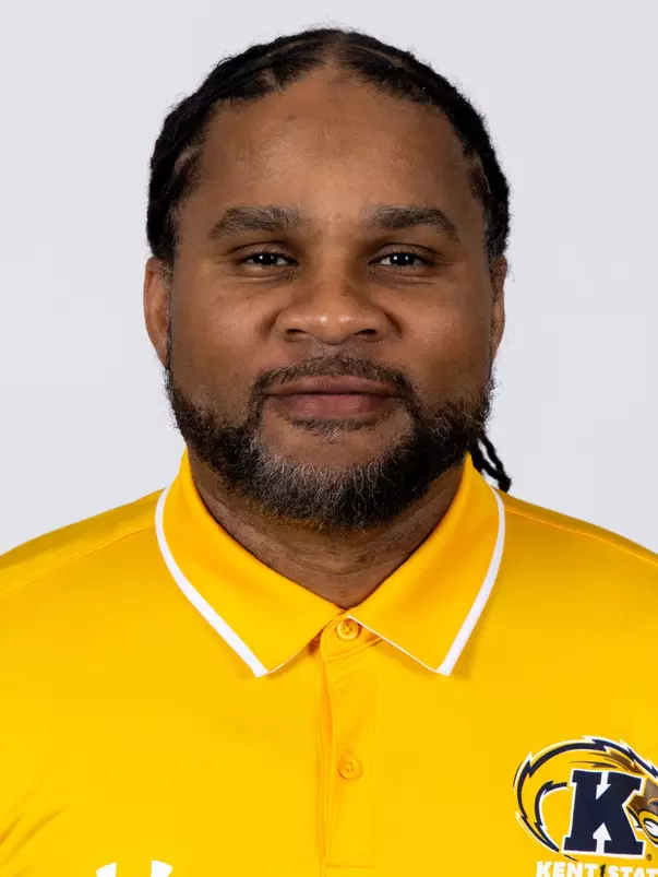 Headshot of Josh Cribbs smiling, wearing a gold Kent State Football Under Armour polo shirt with the Golden Flashes logo and white collar trim, with short dark hair and light stubble.