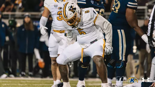 A Kent State football player wearing a white jersey with the number 5 and a white helmet stands on the field during a night game, looking down in a slightly crouched stance.