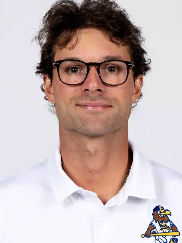 Studio headshot of a young man with dark wavy hair and dark-rimmed glasses, wearing a white Kent State baseball polo shirt against a plain light gray backdrop.