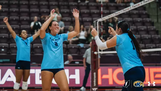 Kent State volleyball players celebrate on the court in front of a mostly empty arena during a match against Virginia Tech.