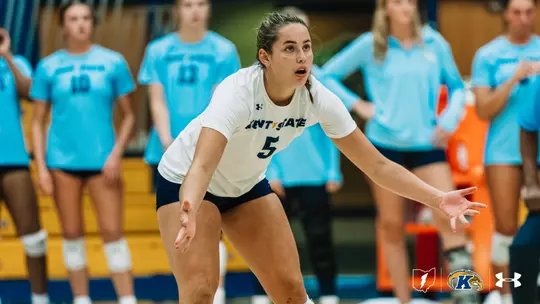 Kent State libero No. 5, wearing white, shuffles into defensive position with arms out, focused on the play in front of her.