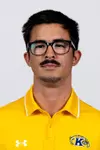 Headshot of a man with short dark hair, glasses, a mustache, and a soul patch wearing a yellow Kent State polo shirt against a plain background.
