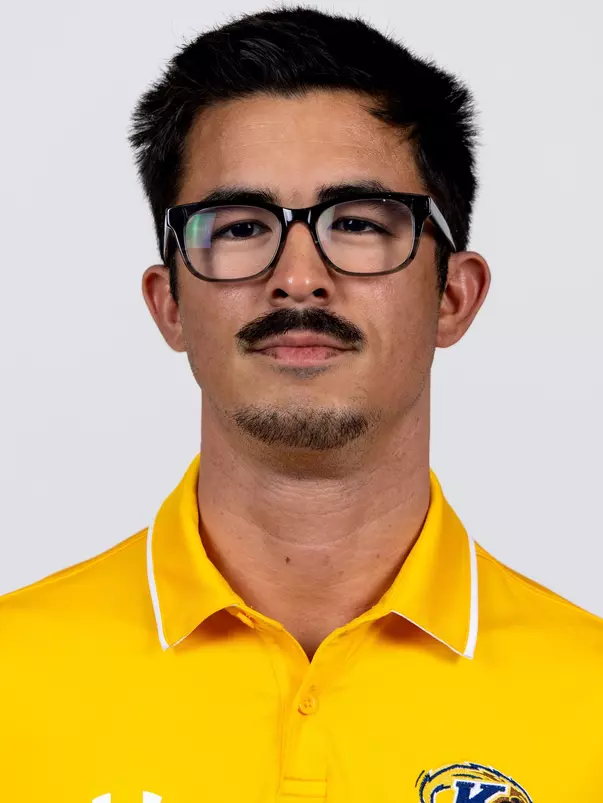 Headshot of a man with short dark hair, glasses, a mustache, and a soul patch wearing a yellow Kent State polo shirt against a plain background.