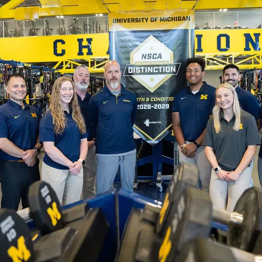 Strength and Conditioning Staff Poses with NCSA College Program of Distinction Banner