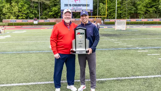 John P. Hardt and Dan Chemotti pose on the field with the Atlantic 10 trophy