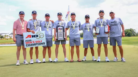 The men's golf team poses on the green after winning the A-10 Championship.