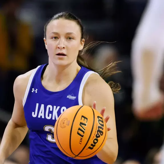 A women's basketball player in a blue uniform dribbles up the court in live action