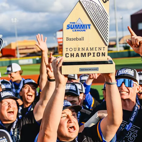 South Dakota State's Luke Luskey hoists the championship trophy at the 2026 Summit League Baseball Championship while his teammates celebrate winning the league tournament around him.