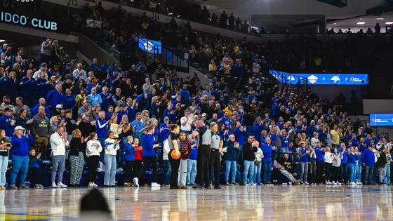A crowd in a basketball arena stands and cheers during a break in on-court action