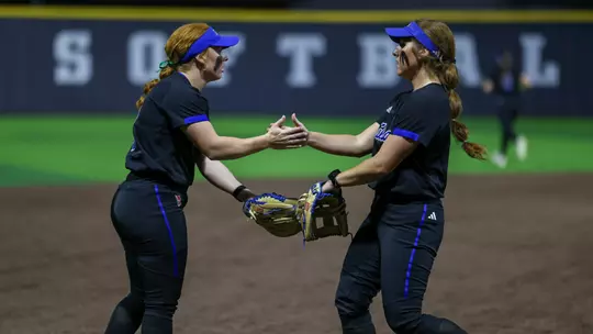 Maci Cole and Claira Skaggs hi-five in the field at Tarleton State