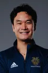 Women's volleyball associate head coach Brandon Thich poses for a head shot in a blue quarter zip with the UCI stacked logo