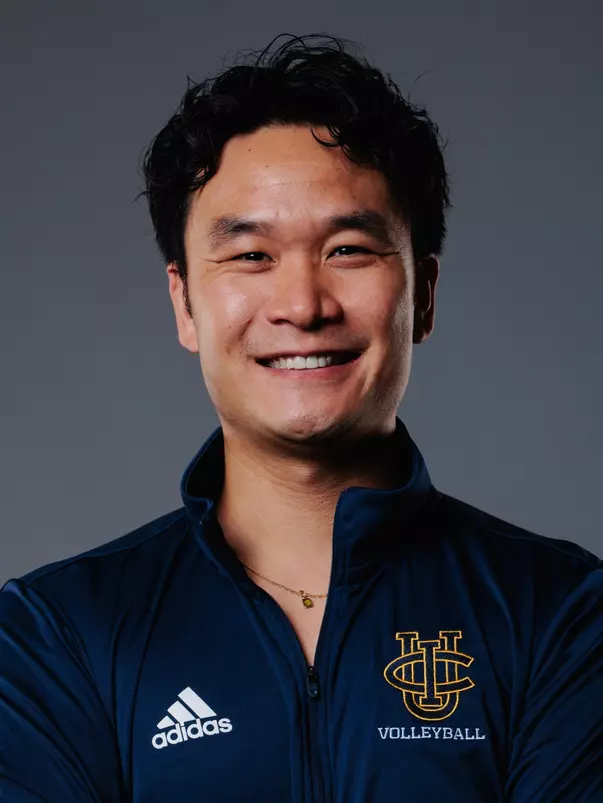 Women's volleyball associate head coach Brandon Thich poses for a head shot in a blue quarter zip with the UCI stacked logo