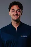 Assistant coach Trevor Briggs poses for a head shot in a blue quarter zip with the text UC Irvine Volleyball