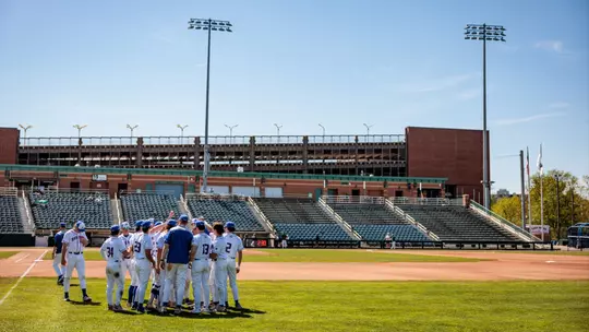 UMass Lowell baseball team in a small huddle on LeLacheur Park pregame