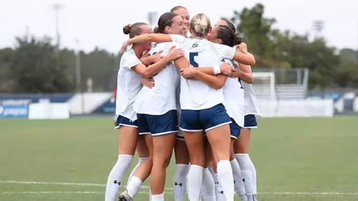 UNF Women's soccer team hugs and celebrates after scoring a goal.