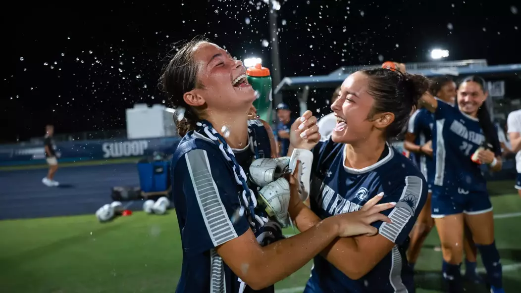 UNF Women's soccer players celebrate a win by pouring water on player.