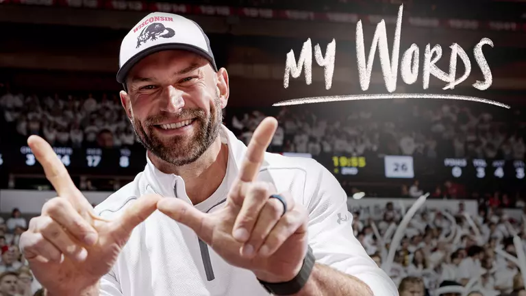 Joe Thomas, Wisconsin football and NFL alumnus, holds his hands in the "W" and smiles with the MyWords logo superimposed over the image