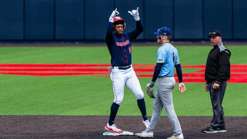 Michael Smith Jr. stands on second base and raises his arms in celebration towards the dugout. He is wearing white pants, a navy jersey and a red helmet.