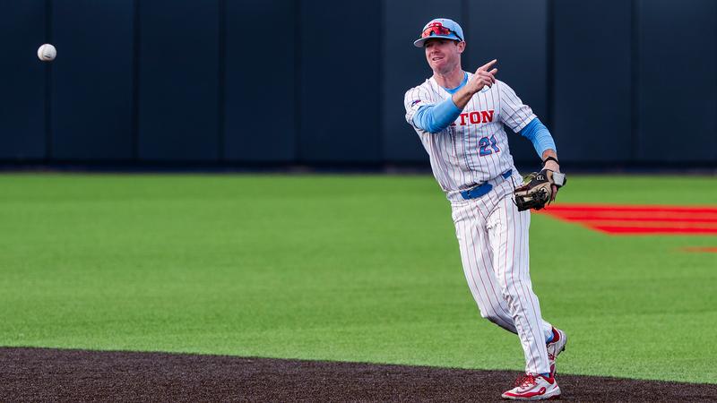 Danny MacDougall throws the ball towards third base. He is wearing a white pinstripe uniform and a chapel blue hat.