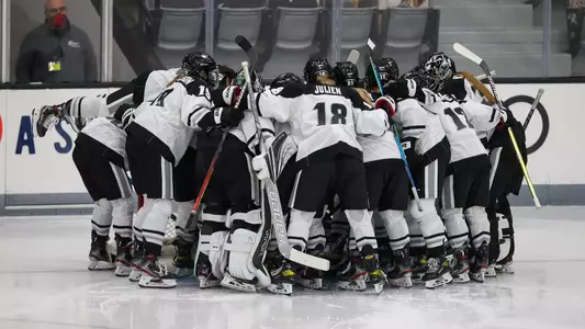 Women's ice hockey team huddling together around the net before the start of a game