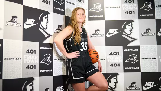 Emily Archibald - women's basketball posed photo in front of media wall