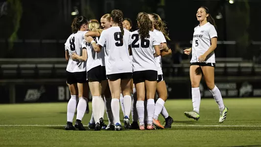 Women's soccer team huddle on Chapey Field at Anderson Stadium. 