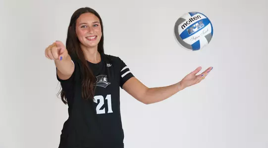 Sophia Adkins poses by throwing the volleyball up with her left hand while she points at the camera with her right arm during team photoshoot for pre-season 2025 photos.