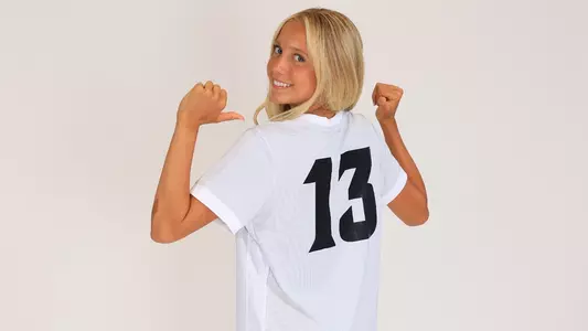 Women's soccer player Sophie Tonino poses for a photo pointing at the back of her jersey during a preseason photoshoot in 2025