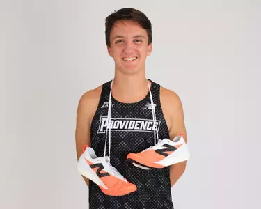 Adam Wedlake smiling at the camera with shoes around his neck