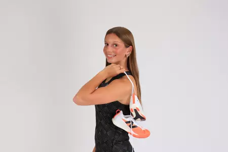 Women's track athlete Morgan Blout poses with her spikes over her shoulder in uniform for media day