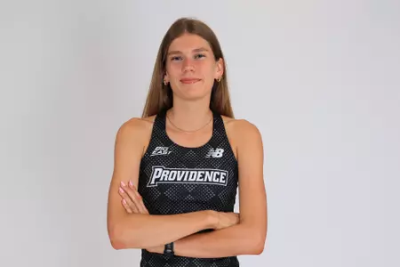 Women's track athlete Kate Currie poses with arms crossed in uniform for media day