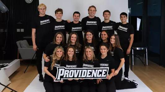 A group photo comprised of the swimming and diving 2025-26 Senior Class holding a Providence word mark logo in front of them.
