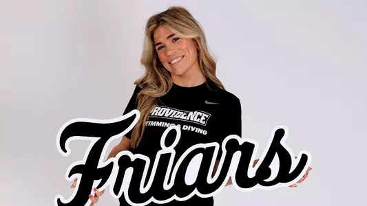 Rylie Foley, dressed in a black Providence College swimming & diving t-shirt, poses with a Friars script word mark in her hands in front of a white back drop.