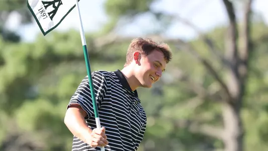 Men's golfer Joe Halferty holding the flag stick and smiling