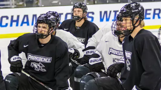 A picture featuring multiple men's hockey player listening to instructions on the ice at practice