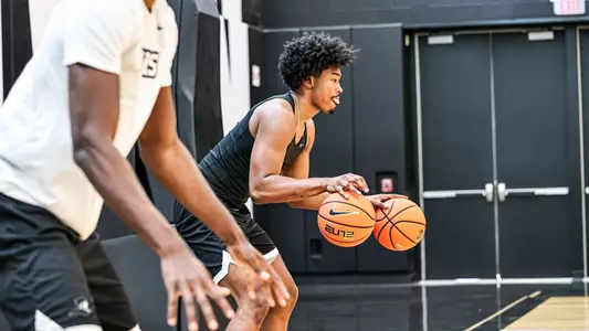 Men's basketball player Jacob Bannarbie dribbling two basketballs on the sideline during a practice