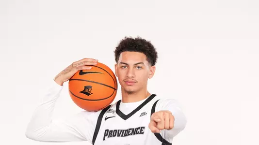 Men's basketball player Miles Byrd posing during an photo shoot with a basketball pointing at the camera