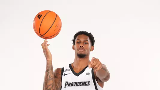 Men's basketball player Devin Vanterpool poses spinning a basketball on his finger and pointing at the camera