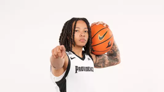 Men's basketball player Malik Mack poses with a basketball on his shoulder and points at the camera during a photo shoot