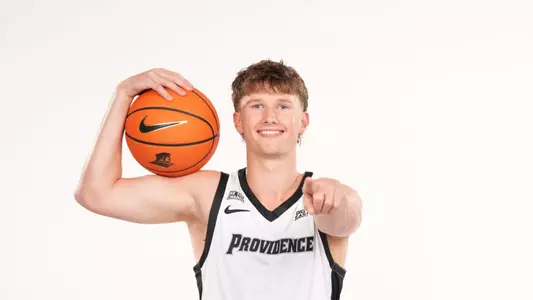 Men's basketball player Ryan Sabol poses with a basketball on his shoulder and points at the camera during a photo shoot