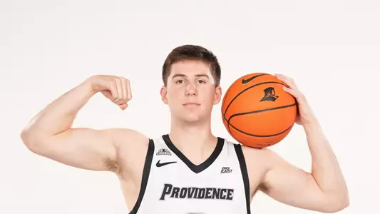 Men's basketball player Ryan Mela poses with a ball on his shoulder and flexing his arm during a photo shoot
