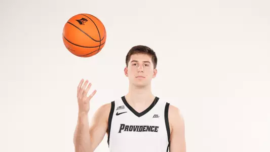 Men's basketball player Ryan Mela poses throwing a basketball into the air during a photo shoot