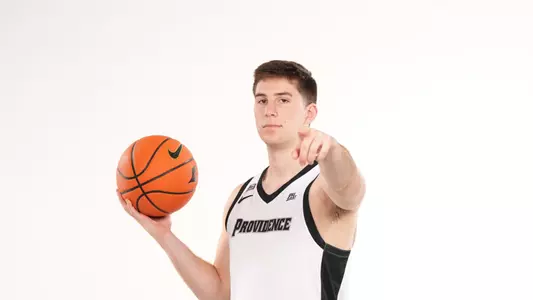 Men's basketball player Ryan Mela poses with a basketball in his hand and points at the camera during a photo shoot
