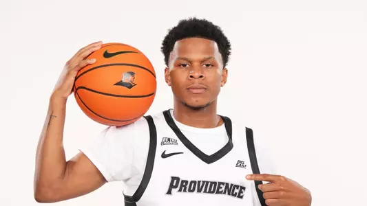 Men's basketball player Gavin Hightower pointing at the Providence logo during a photoshoot