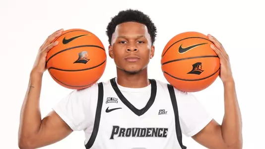 Men's basketball player Gavin Hightower holding two basketballs on his shoulder during a photoshoot