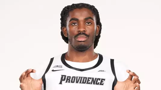 Men's basketball player Samson Aletan posing for a photo while flexing the Providence jersey