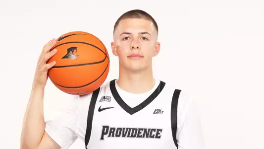 Men's basketball player John Jackson posing for a photo with a basketball on his shoulder